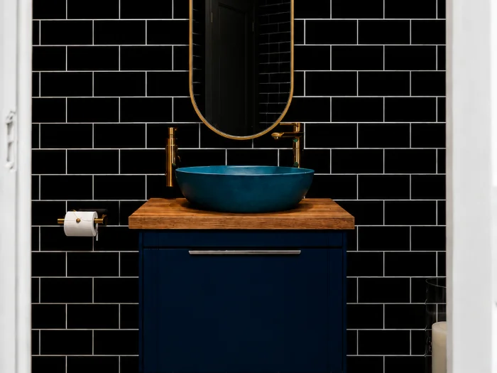 The bathroom downstairs in the studio: black subway tile, a blue vessel sink and gold tapware