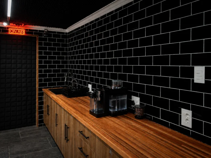 The downstairs coffee bar: black subway tile, a wood counter with sink and coffee machine, ON AIR sign above the door