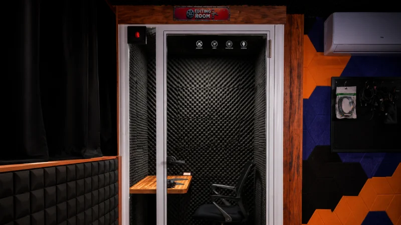 The soundproof editing booth, a glass-doored isolation pod with acoustic foam, a fold-down desk and headphones