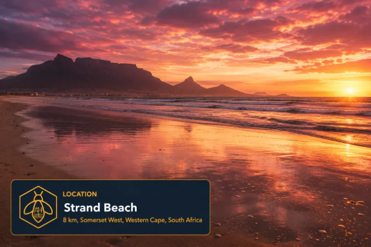 A wide sandy beach at sunset with mountains across the bay