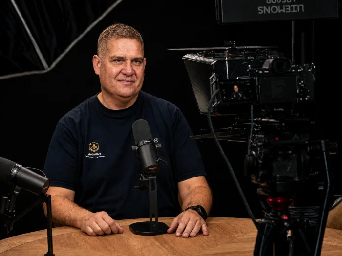 Mr Bee, AutoHive's founder, seated at the studio table against the black backdrop
