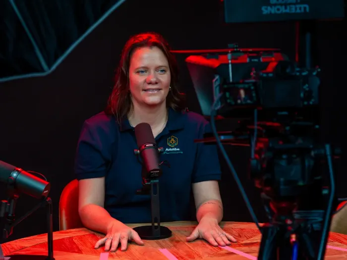 A host seated at the studio table against the black backdrop, lit red
