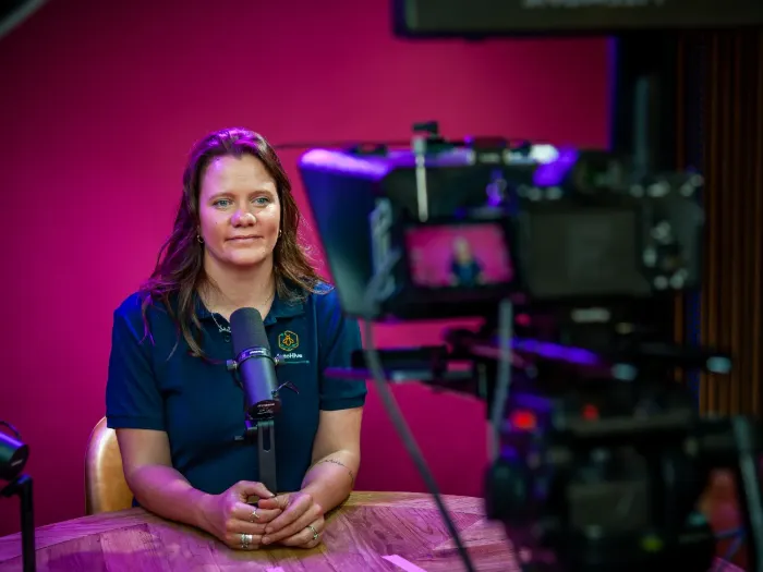 A host seated at the studio table against the pink backdrop