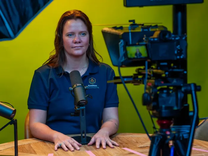 A host seated at the studio table against the yellow backdrop